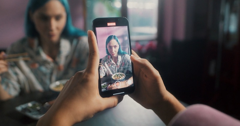 Person recording a woman with blue hair eating at a restaurant, showcasing content creation for digital creators